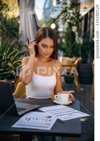 Break time, with coffee. Beautiful young woman is outdoors of the restaurant by the table Break time, with coffee. Beautiful young woman is outdoors of the restaurant by the table 134380528