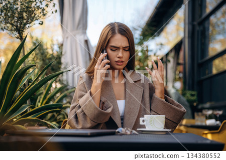With smartphone. Beautiful young woman is outdoors of the restaurant by the table 134380552