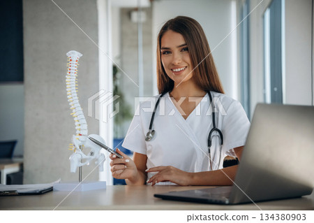 Spine model on the table. Professional female doctor in the clinic indoors Spine model on the table. Professional female doctor in the clinic indoors 134380903