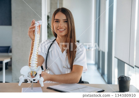 Spine model on the table. Professional female doctor in the clinic indoors Spine model on the table. Professional female doctor in the clinic indoors 134380910
