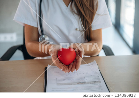 Close up view, holding little red heart. Professional female doctor in the clinic indoors 134380928