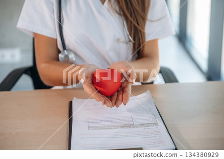 Close up view, holding little red heart. Professional female doctor in the clinic indoors 134380929