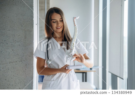 Holding spine model. Professional female doctor in the clinic indoors 134380949