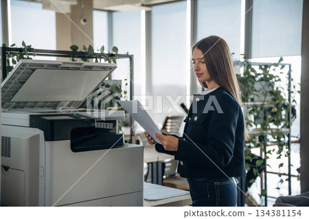 Working with printer. Beautiful woman is in the office 134381154