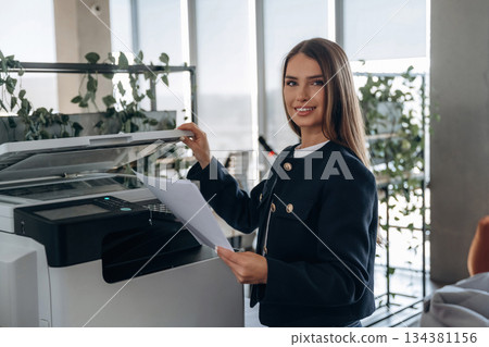 Working with printer. Beautiful woman is in the office Working with printer. Beautiful woman is in the office 134381156