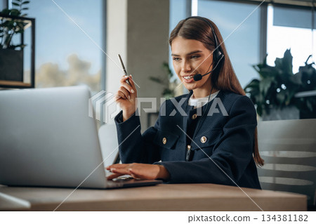 Advice, using laptop and headphones, talking. Woman is working in the office Advice, using laptop and headphones, talking. Woman is working in the office 134381182