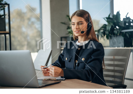 Answering the call, in headphones. Woman is working in the office Answering the call, in headphones. Woman is working in the office 134381189