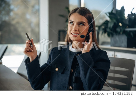 Answering the call, in headphones. Woman is working in the office Answering the call, in headphones. Woman is working in the office 134381192