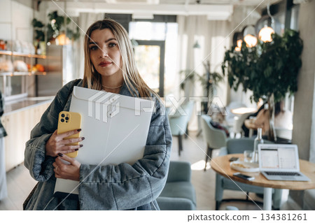 Woman with smartphone and paper package is standing indoors 134381261