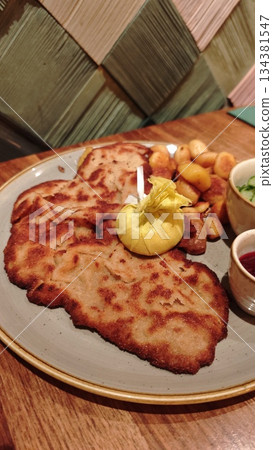 German schnitzel with crispy breaded meat served with fried potatoes, lemon and sauces on a restaurant plate. Concept of traditional German cuisine, hearty comfort food and classic European dining 134381547