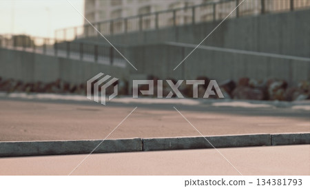 A group of skateboarders performs tricks on a smooth concrete surface as the sun sets behind modern buildings. The warm glow creates a vibrant atmosphere for the evening skate session. A group of skateboarders performs tricks on a smooth concrete surface as the sun sets behind modern buildings. The warm glow creates a vibrant atmosphere for the evening skate session. 134381793