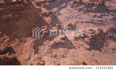 A breathtaking scene captures the intricate formations of deep canyons in a vast desert. The landscape is bathed in bright sunlight, highlighting every detail of the rocky terrain. 134381860
