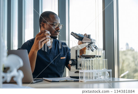 Bunch of test tubes. Scientist is working indoors, microscope is on the table Bunch of test tubes. Scientist is working indoors, microscope is on the table 134381884