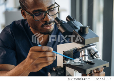 Focused on job. Scientist is working indoors, microscope is on the table Focused on job. Scientist is working indoors, microscope is on the table 134381902