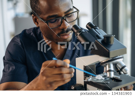 Focused on job. Scientist is working indoors, microscope is on the table Focused on job. Scientist is working indoors, microscope is on the table 134381903