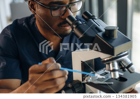 Focused on job. Scientist is working indoors, microscope is on the table Focused on job. Scientist is working indoors, microscope is on the table 134381905
