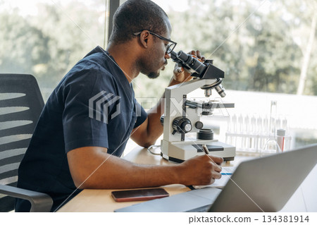 Near the window. Scientist is working indoors, microscope is on the table Near the window. Scientist is working indoors, microscope is on the table 134381914