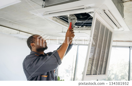 Ventilation is on the ceiling, fixing it. Repairman is indoors in the modern office 134381932