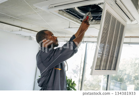 Ventilation is on the ceiling, fixing it. Repairman is indoors in the modern office 134381933