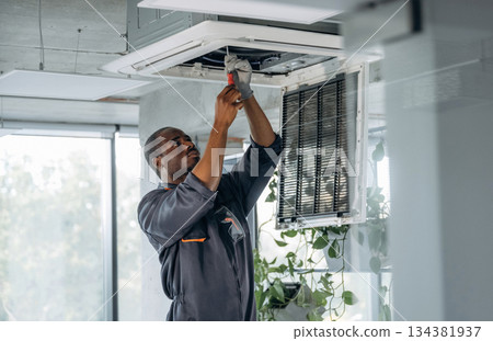 High up, fixing the ventilation. Repairman is indoors in the modern office 134381937