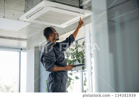 High up, fixing the ventilation. Repairman is indoors in the modern office High up, fixing the ventilation. Repairman is indoors in the modern office 134381939