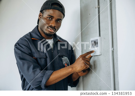 Examining the thermostat. Repairman is indoors in the modern office Examining the thermostat. Repairman is indoors in the modern office 134381953