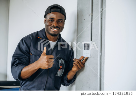 Examining the thermostat. Repairman is indoors in the modern office 134381955
