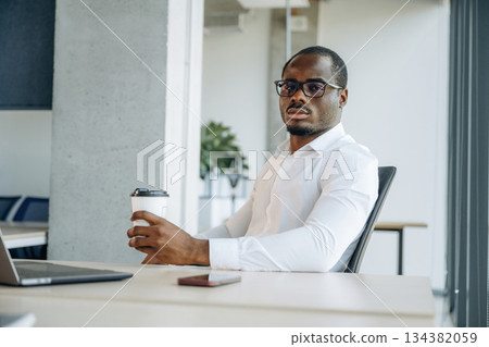 With drink in hand, by table. Businessman is working in modern office With drink in hand, by table. Businessman is working in modern office 134382059