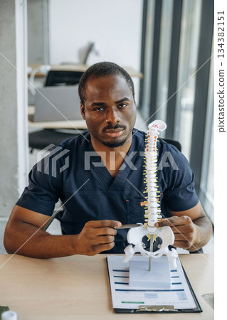 Table with human spine model on it. Professional doctor is in his office indoors 134382151