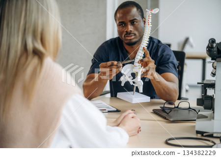 Female patient is at consultation with doctor. Man is showing spine model, problems with back 134382229