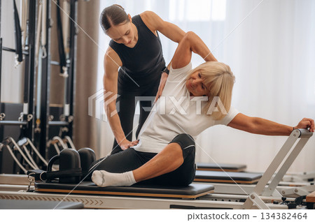 Exercise for the back. Female trainer is helping old woman Exercise for the back. Female trainer is helping old woman 134382464