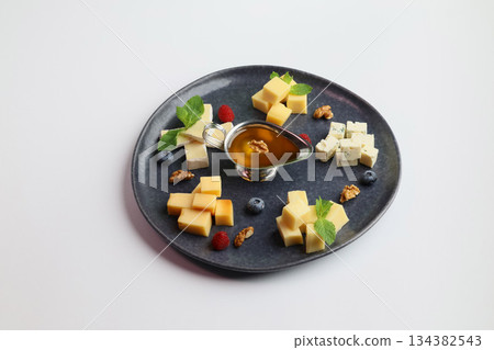 Cheese assortment on big dark plate with honey on white background Cheese assortment on big dark plate with honey on white background 134382543