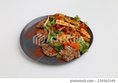 Salad with grilled veal and vegetables on a dark plate on a white background, restaurant serving Salad with grilled veal and vegetables on a dark plate on a white background, restaurant serving 134382549
