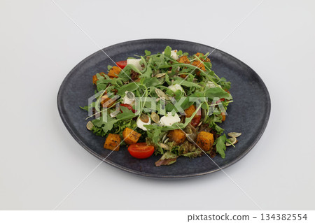Grilled pumpkin salad with arugula and pumpkin seeds with oil on dark plate on a white background Grilled pumpkin salad with arugula and pumpkin seeds with oil on dark plate on a white background 134382554