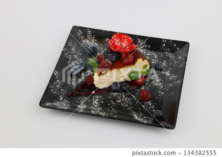Tasty cheesecake with berries and sauce on a black plate on a white background Tasty cheesecake with berries and sauce on a black plate on a white background 134382555