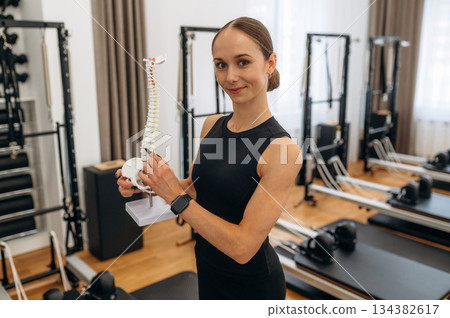 Human spine model in hands. Young woman is in the gym with training equipment Human spine model in hands. Young woman is in the gym with training equipment 134382617