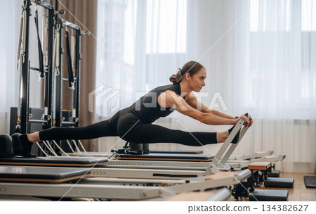 Side view, doing exercises. Young woman is in the gym with training equipment Side view, doing exercises. Young woman is in the gym with training equipment 134382627