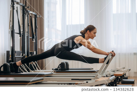 Side view, doing exercises. Young woman is in the gym with training equipment 134382628