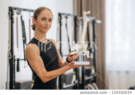 Showing the bones of the model of spine. Young woman is in the gym with training equipment 134382634