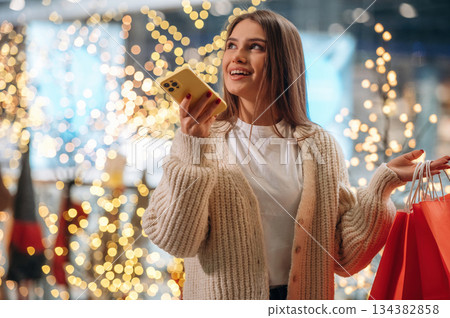 Magical decorations, talking by phone. New year shopping and presents. Woman is near the Christmas tree 134382858