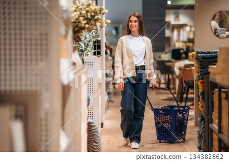 Blue basket is on the floor. Woman is in the shop with decoration, indoors Blue basket is on the floor. Woman is in the shop with decoration, indoors 134382862