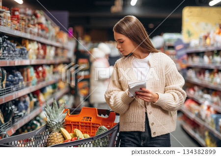 Shelves with products. Beautiful woman is in the supermarket 134382899