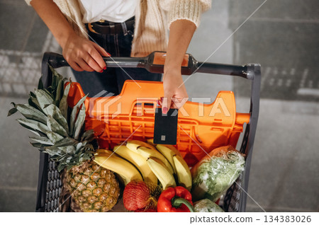 Close up view of shopping cart with fruits and vegetables, woman is standing 134383026