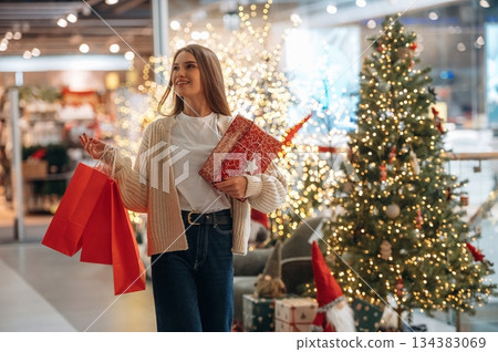 Gift in hands. New year shopping and presents. Woman is near the Christmas tree Gift in hands. New year shopping and presents. Woman is near the Christmas tree 134383069