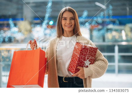Cheerful facial expression, standing. New year shopping and presents. Woman is near the Christmas tree Cheerful facial expression, standing. New year shopping and presents. Woman is near the Christmas tree 134383075