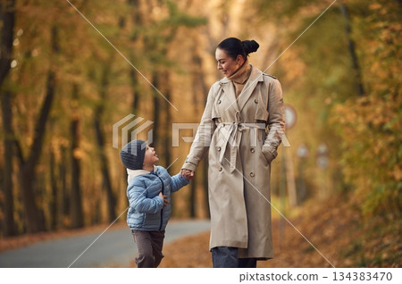 Mother with her son are having a walk in autumn forest near the road 134383470