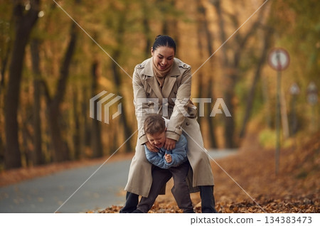 Fun times, behind the boy. Mother with her son are having a walk in autumn forest near the road Fun times, behind the boy. Mother with her son are having a walk in autumn forest near the road 134383473