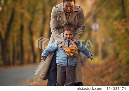 Fun times, behind the boy. Mother with her son are having a walk in autumn forest near the road 134383474