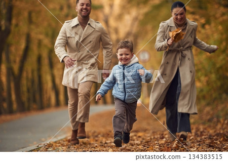 Boy is running forward. Happy family are together in the autumn forest near the road 134383515