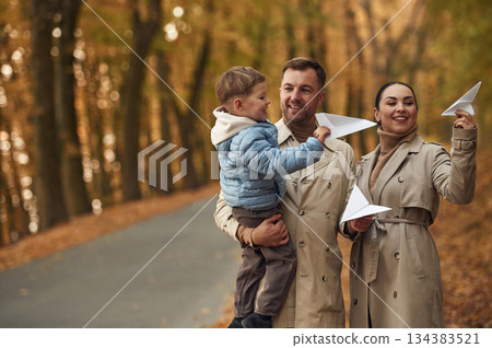 With paper planes. Happy family are together in the autumn forest near the road With paper planes. Happy family are together in the autumn forest near the road 134383521